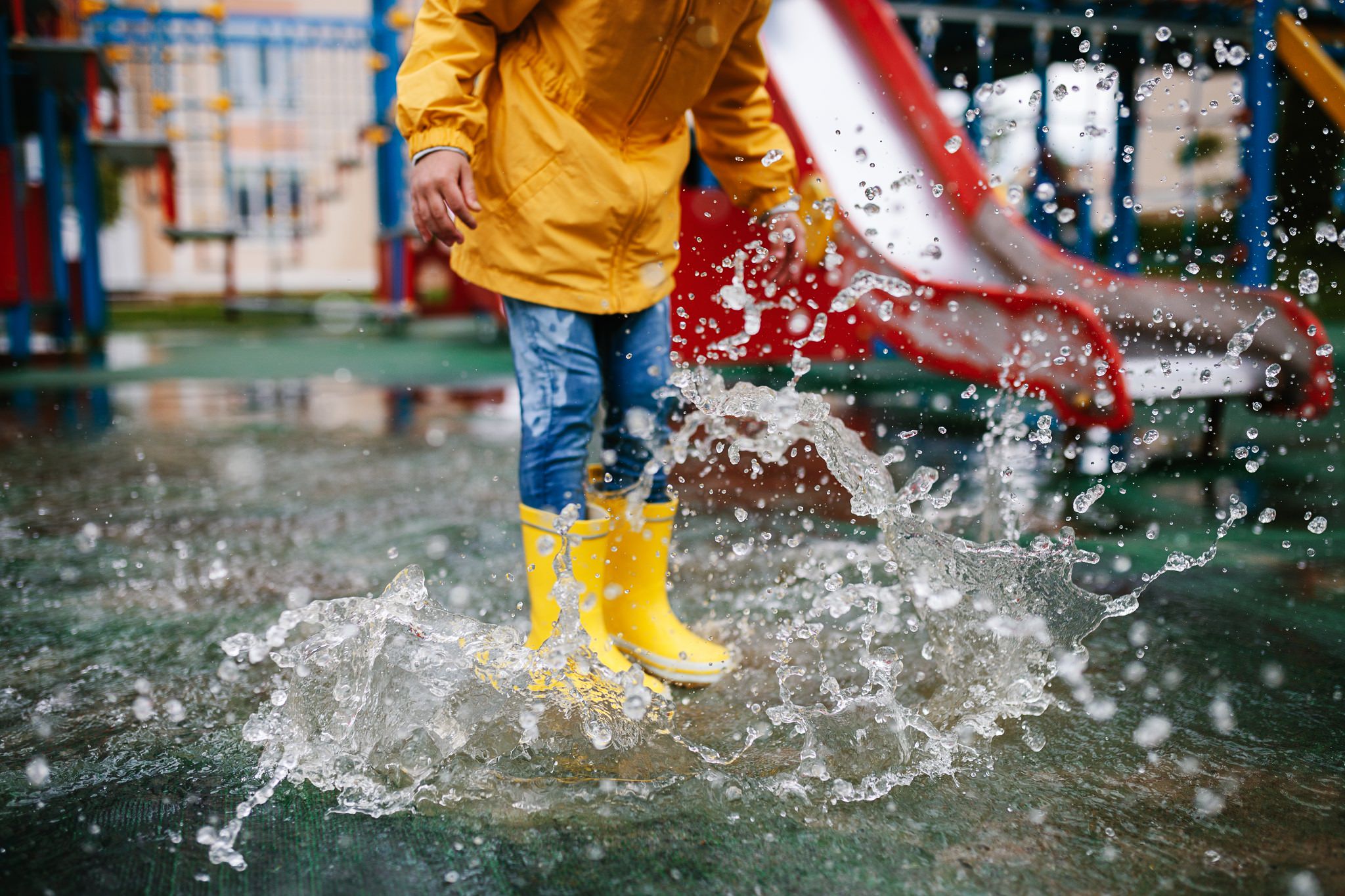 Un enfant saute dans une flaque d'eau avec un ciré et des bottes jaunes.