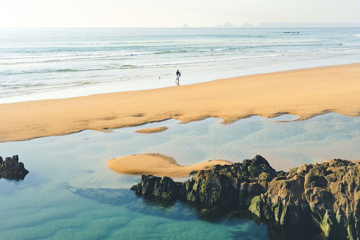 Surfeur sur la plage de la Palue et vue sur la Pointe du Raz sur la presqu'île de Crozon (Finistère)